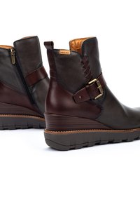 Botas de tobillo de cuero con un exterior gris oscuro, detalles marrones, una cremallera lateral y una hebilla decorativa con un tacón en cuña.