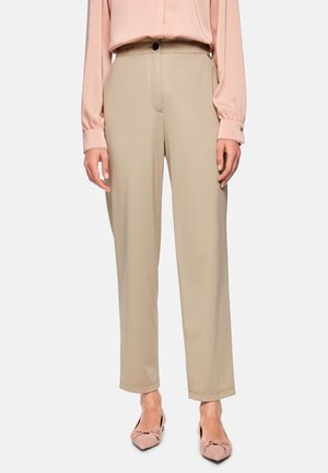 Beige tailored trousers with a smooth texture, slightly loose fit, and a button closure at the waist, paired with pink silk blouse and pink flats.
