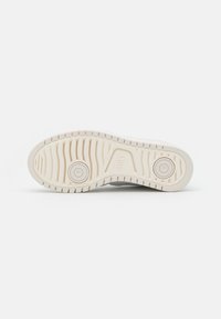 White sneaker sole with textured grip pattern, featuring two circular indents and a smooth, raised logo section in the center.