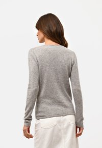 Grijze wollen trui met lange mouwen en een ronde hals, met een gladde textuur en een aansluitende pasvorm. Witte rok zichtbaar eronder.