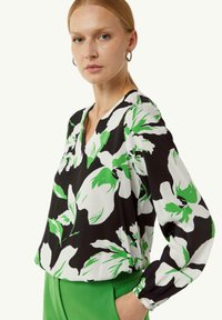 Blumenbluse in Schwarz, Weiß und Grün, mit langen Ärmeln und V-Ausschnitt. Hat einen lockeren Schnitt und geraffte Ärmelbündchen.