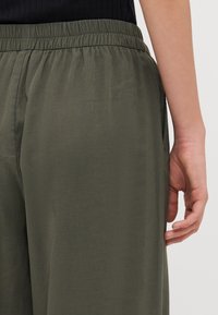 Olive green trousers with an elastic waistband and side pockets, featuring a soft texture and relaxed fit designed for comfort.
