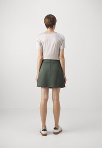 Grønn skjørt med en tettsittende midje og flagrende kant, kombinert med en lysfarget topp med korte ermer. Skotøyet består av hvite joggesko med grønne accenter.