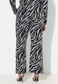 Zwart en zilver zebraprint wijde broek met een gladde textuur en elastische tailleband, gecombineerd met zilveren hoge hakken.