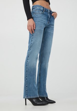 Jeans svasati blu chiaro in denim con finitura sbiadita, caratterizzati da un design a cinque tasche e un orlo dritto, abbinati a tacchi neri.