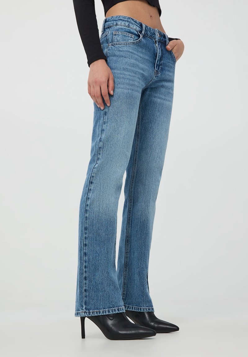 Jeans svasati blu chiaro in denim con finitura sbiadita, caratterizzati da un design a cinque tasche e un orlo dritto, abbinati a tacchi neri.
