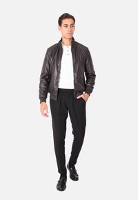 Giacca bomber in pelle nera con polsini a coste, abbinata a pantaloni neri sartoriali e una maglietta henley bianca. Presenta una chiusura con zip.