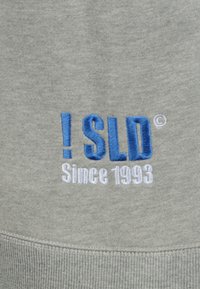 Siva dukserica s plavim izvezenim tekstom koji glasi "! SLD" i "Od 1993.", izrađena od mekog materijala s rebrastim manžetama na dnu.