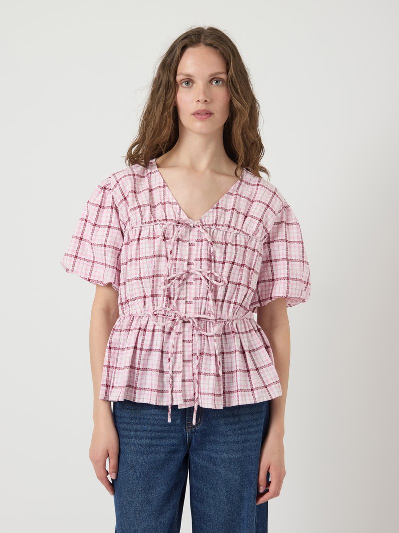 Top peplum a scacchi rosa e bianchi con scollatura a V, maniche a palloncino e dettagli con cordoncino in vita. Realizzato in tessuto leggero.