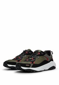 Chaussures de sport présentant un design noir, vert et rouge avec une tige texturée, une semelle blanche épaisse et une semelle extérieure en caoutchouc noir durable.