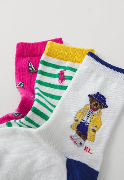 Tre par färgglada strumpor: rosa med segelbåtar, gröna och vita ränder med en logotyp, och vita med en björn i gul kappa.