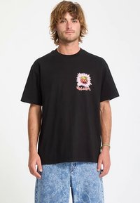 Musta puuvillainen t-paita, jossa on lyhyet hihat ja värikäs hirviökuvio vasemmassa rinnassa. Yhdistetty vaaleansinisiin farkkuihin.