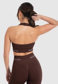 Top corto marrón de canalé con escote halter, combinado con leggings de talle alto que presentan una marca blanca. Textura suave, diseño ajustado.