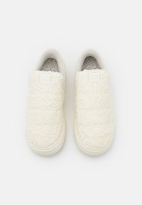 Biele nadýchané šľapky s textúrovaným zvrškom, zaoblenou špičkou a gumovou podrážkou. Majú minimálne logo a mäkké vnútorné podšívku.