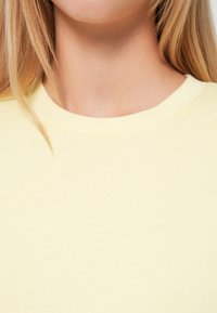 Geltona medvilninė marškinėlių su apvalia iškirpte, švelnios tekstūros ir prigludusio kirpimo, demonstruojanti lygaus audinio paviršių be raštų ar puošmenų.