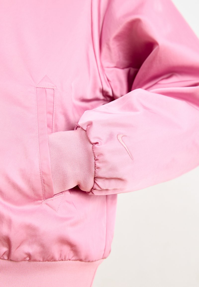 Rosa Bomberjacke aus glattem Stoff, mit gerippten Bündchen, einer Seitentasche und einem kleinen gestickten Logo am Ärmel.