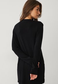 Zwarte lange mouwen cardigan met een ontspannen pasvorm, gladde textuur en zijzakken. Heeft een ronde halslijn en geribde manchetten en zoom.