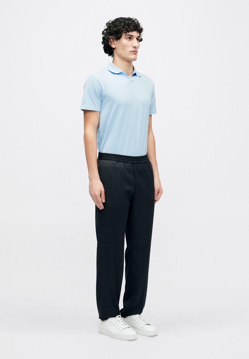 Hellblaues Poloshirt mit kurzen Ärmeln, kombiniert mit schwarzen Hosen mit elastischem Bund und weißen Turnschuhen. Einfaches Design mit lockerer Passform.