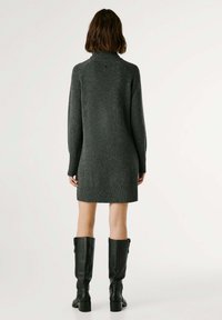 Vestito maglione grigio con colletto alto, polsini e orlo a coste. Un paio di stivali in pelle neri al ginocchio. Design minimalista.