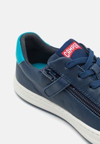 Navy lädersneakers med vit sula, med en siddragkedja, blå accenter och en röd CAMPER-logotyp på tungan.