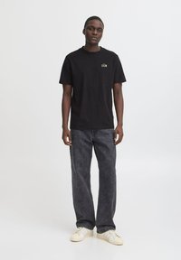 Svart bomulls t-skjorte med "CALM" trykt i gull, kombinert med mørk grå denim jeans og hvite sneakers med lys grå detaljer.