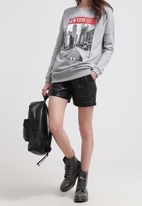 Sweat-shirt gris avec graphique "New York City", shorts noirs en simili cuir, bottes grises à lacets, et sac à dos noir. Design simple et moderne.