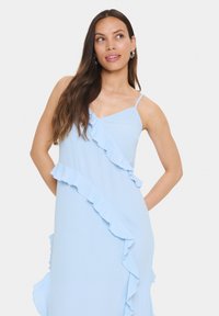 Rochie bleu deschis dintr-un material moale, având un detaliu de volan în diagonală pe față și bretele subțiri ajustabile.