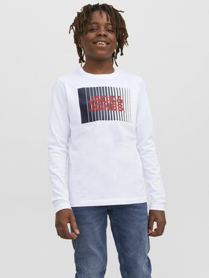 Witte longsleeve t-shirt met een centraal grafisch ontwerp met marineblauwe en rode tekst op een gestreepte achtergrond. Draagt het met blauwe spijkerbroek.