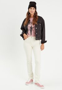 Veste en denim noir, t-shirt graphique rose, pantalon crème et baskets roses. La tenue présente une coupe décontractée avec un style casual.