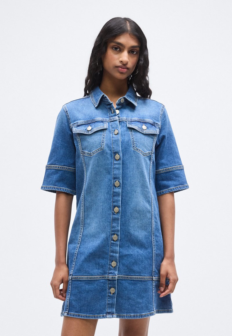Φόρεμα πουκάμισο από τζιν με γιακά, κοντά μανίκια, τσέπες στο στήθος και κλείσιμο με κουμπιά. Ανοιχτό μπλε χρώμα με λεπτομέρειες ραφής και άνετη εφαρμογή.
