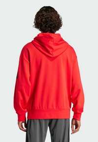 Röd hoodie med en stor huva, ribbade ärmslut och fåll. Tillverkad av mjukt tyg, har en minimalistisk design utan synliga logotyper eller mönster.