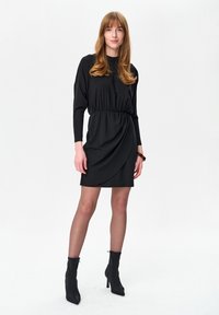Czarna sukienka z długimi rękawami, taliowana, z drapowanym przodem i sięgającym do kolan dołem. W połączeniu z czarnymi, szpiczastymi botkami na kostkę. Gładka tekstura materiału.