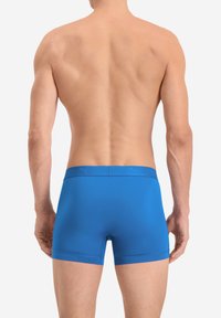 Blaue Boxershorts mit glatter Textur und einem elastischen Bund, der erhabene Logodetails aufweist. Sicht von hinten auf einen nackten Oberkörper.