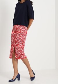 Marinblå kortärmad tröja lager-på-lager över en röd blyertskjol med ett vitt och rosa blommönster. Har en slits framtill och blå klackskor.