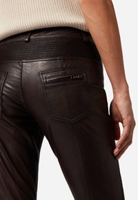 Bruine leren broek met een geribde tailleband, schuine zakken en een ritszak aan de achterkant, met een gladde textuur en een getailleerde pasvorm.
