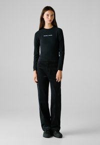 Haut noir à manches longues avec le texte "RED BULL RACING", associé à un pantalon en velours côtelé noir ample et des chaussures noires.