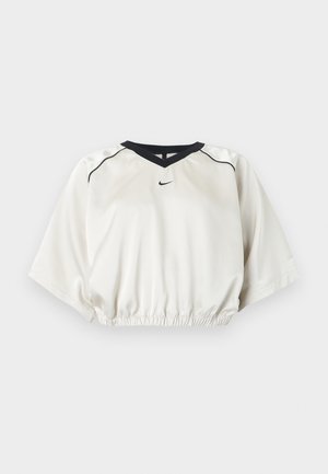 Λευκό κοντό αθλητικό τοπ με μαύρο περίγραμμα στο λαιμό σε σχήμα V, ελαστική μέση, κοντά φαρδιά μανίκια και μικρό μαύρο λογότυπο Nike στο μπροστινό κέντρο.