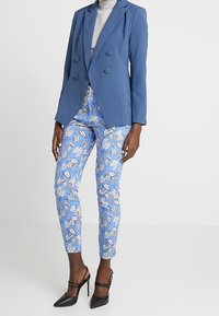 Light blue tailored blazer with double-breasted buttons, paired with patterned light blue trousers featuring floral prints and black high-heeled shoes.
