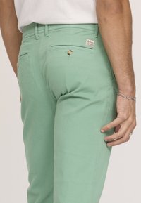Pantalons en coton vert menthe avec une coupe slim, dotés de poches arrière avec fermeture à bouton et d'une étiquette sur la taille.