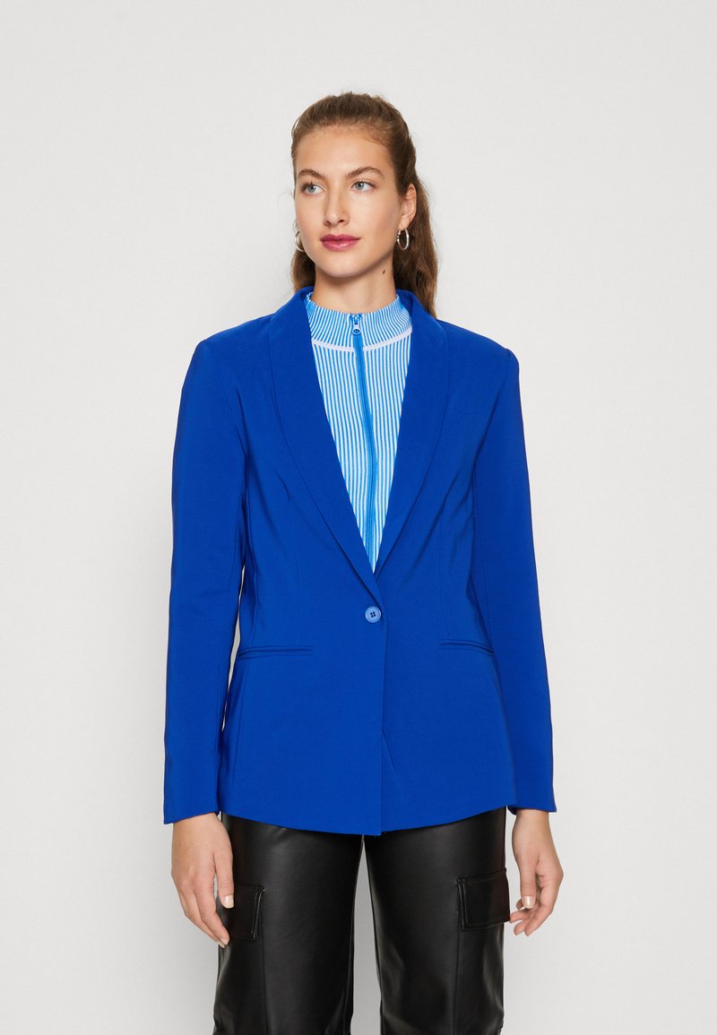 Blazer azul real con mangas largas, cierre de un solo botón y cuello con solapa, combinado con una blusa de rayas azules y blancas y pantalones negros.