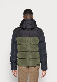 Puffet jakke med en sort og olivengrøn farveblokdesign, med hætte og quiltet tekstur, sikret med elastiske ærmer.