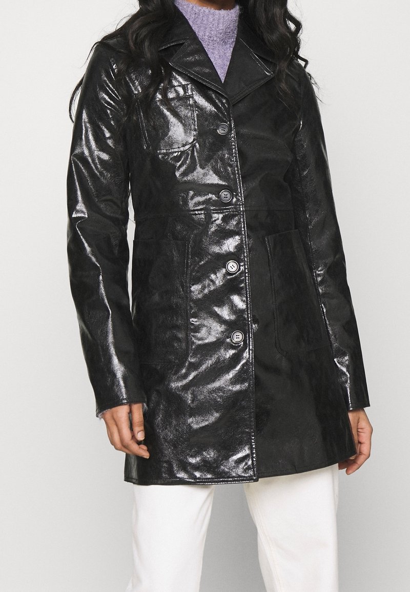 Manteau noir brillant à coupe ajustée, fermeture à boutons, poches à rabat et col cranté. Fabriqué en matériau brillant, design mi-longueur.