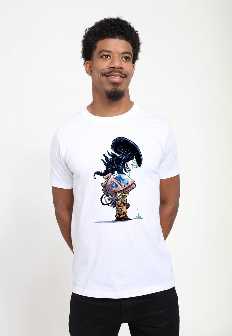 Muž v bílém tričku s kresleným motivem astronauta a mimozemského tvora obracejících se k sobě, oba kape z nich tekutina.