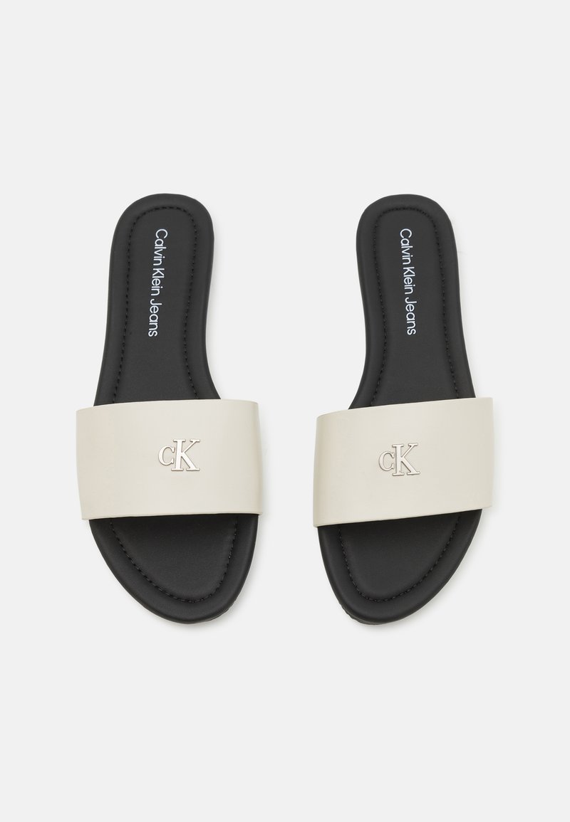 Chanclas Calvin Klein con una amplia correa en color blanco sucio, planta negra y detalle de logotipo en relieve. Material suave con un diseño plano.