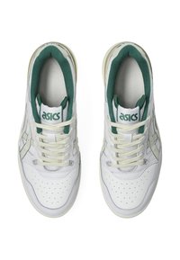 White sneakers with green accents, featuring a perforated toe, laces, and logo. Leather upper with textile lining and a rubber sole.