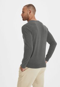 Grauer Langarmpullover mit rundem Ausschnitt, aus weichem Strickstoff, mit gerippten Bündchen und Saum, getragen mit beigen Hosen.