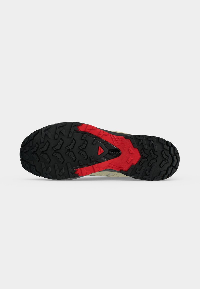 Semelle en caoutchouc noire et rouge, robuste, d'une chaussure de randonnée avec des crampons profonds pour accroche sur terrain accidenté.