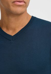 Tume sinise V-kaelusega sviiter, mis on valmistatud siledast, kudumisest materjalist. Omab soonikservaga kaelust ja pehmet tekstuuri, rõhutades vormistatud disaini.