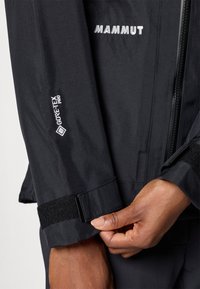 Must mustriga, mis sisaldab GORE-TEX Pro tehnoloogiat. Tuntud omadused hõlmavad Velcro manseti reguleerimist ja peegelduvaid logo aktsente.