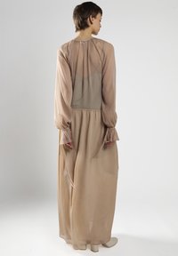 Langes, beiges Kleid aus durchscheinendem Material mit voluminösen Ärmeln, gerafften Details an den Schultern und einem ausgestellten Saum. Der Rücken hat ein Netzpaneel.